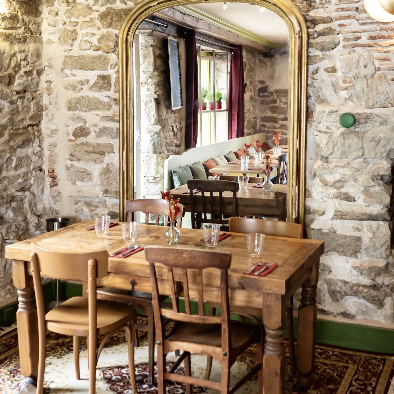 Table de 4 personnes en mobilier chiné devant un mur en pierre avec un ancien miroir patiné