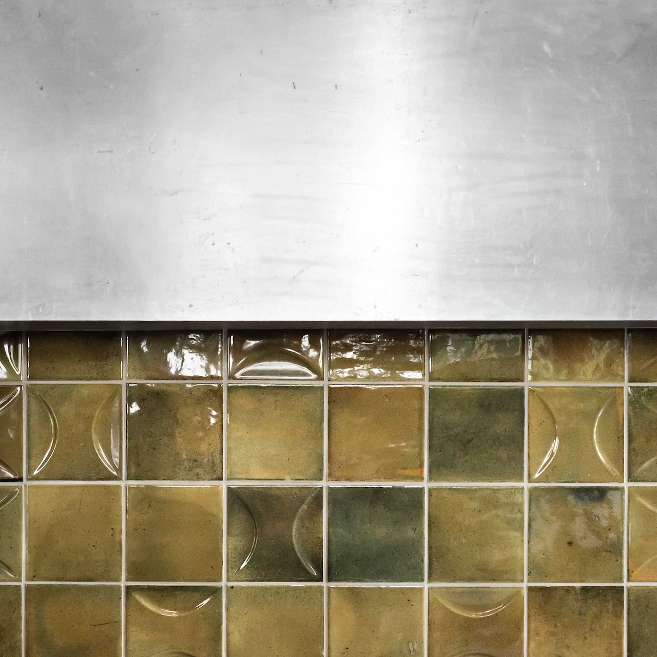 Zoom sur faïence verte mixée avec carreaux lisses et texturés en demi-lune, associée au plan de bar en zinc existant