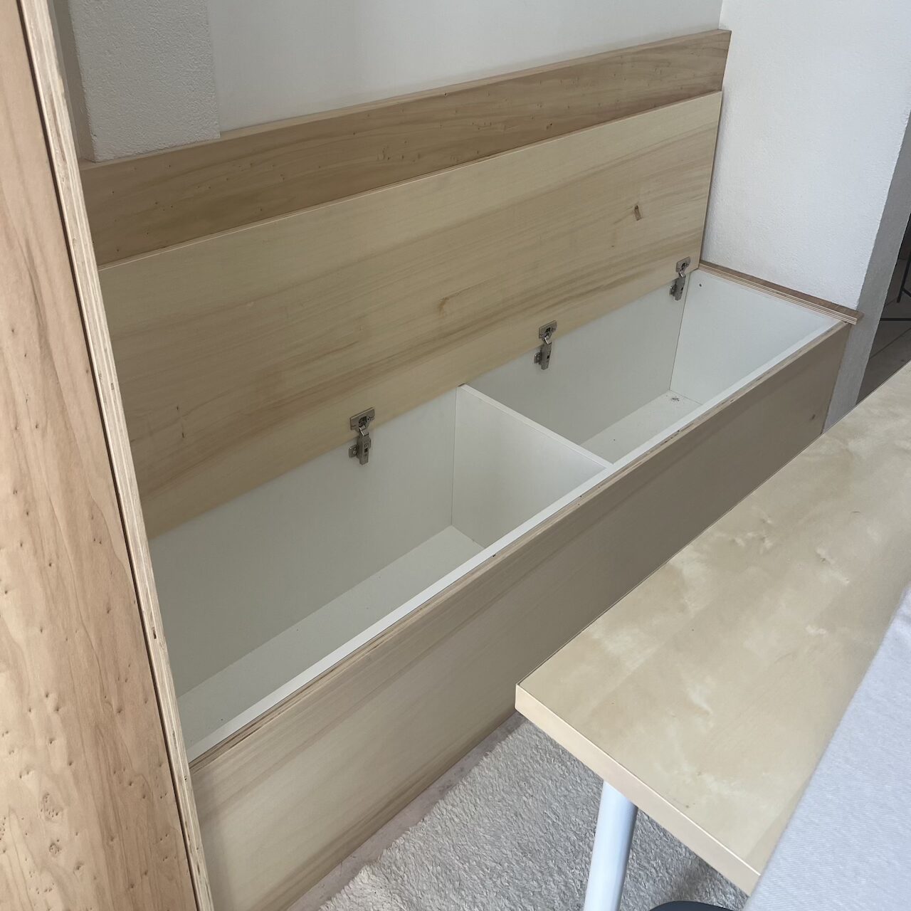 Vue de la banquette en contreplaqué avec coffre ouvert pour maximiser le rangement dans un loft à Nantes