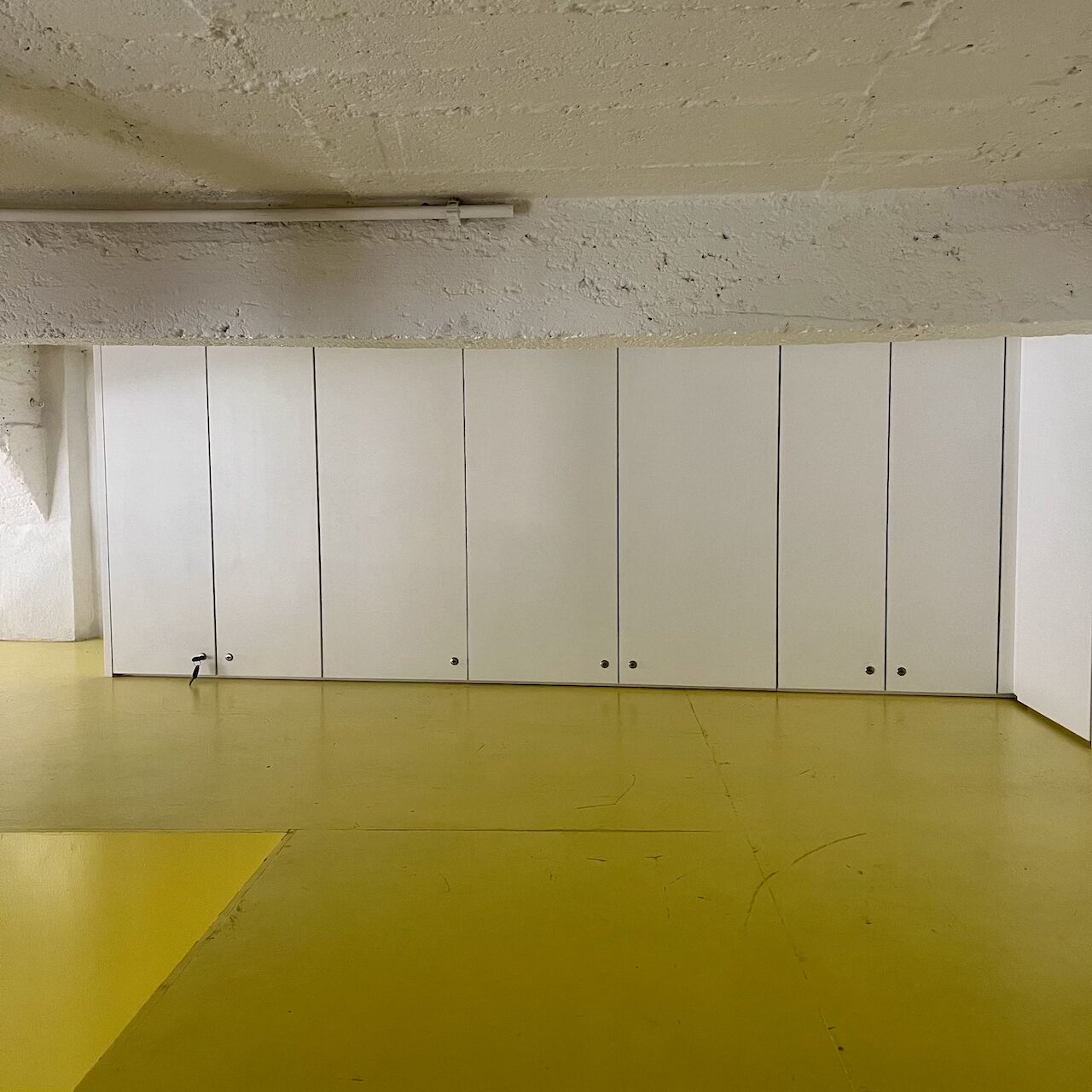 Meubles de rangement sur mesure intégrés autour du bloc jaune et sous les poutres dans un loft brut à Nantes