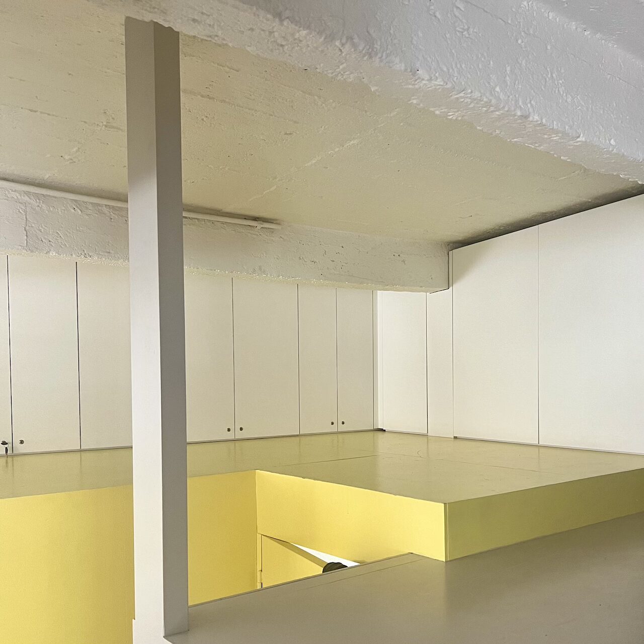 Meubles de rangement sur mesure intégrés autour du bloc jaune et sous les poutres dans un loft brut à Nantes