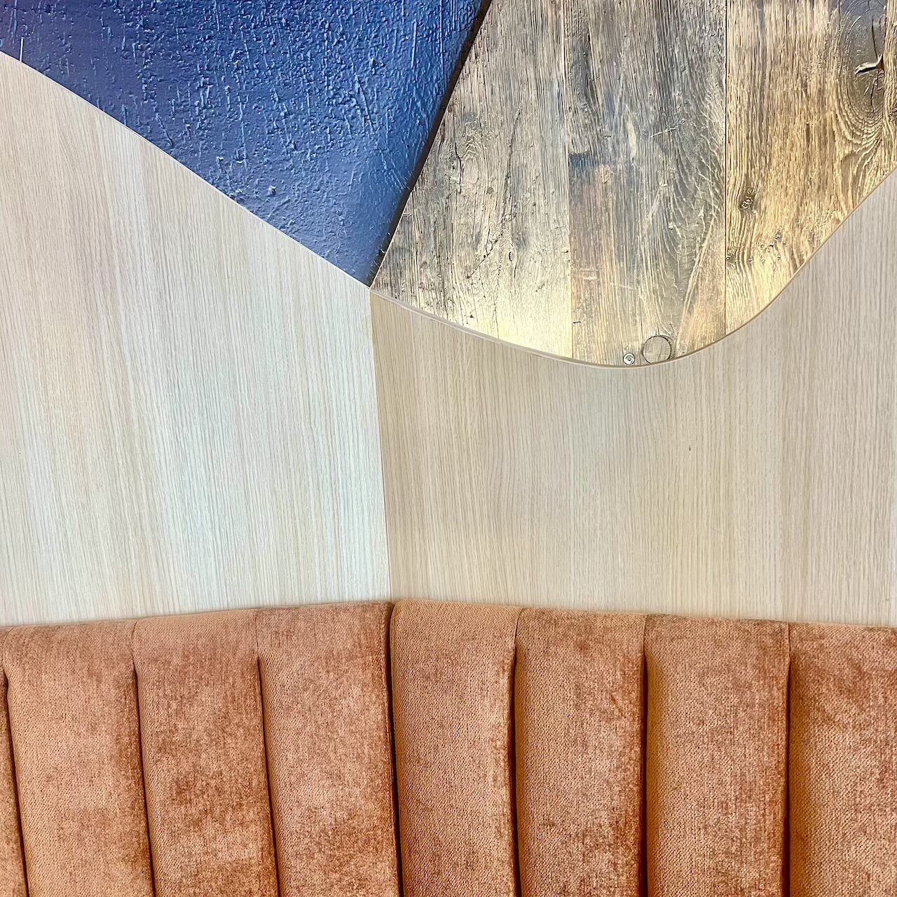 Gros plan sur les matériaux de la banquette en velours terracotta et l’habillage bois mêlant stratifié et bois brut rétroéclairé