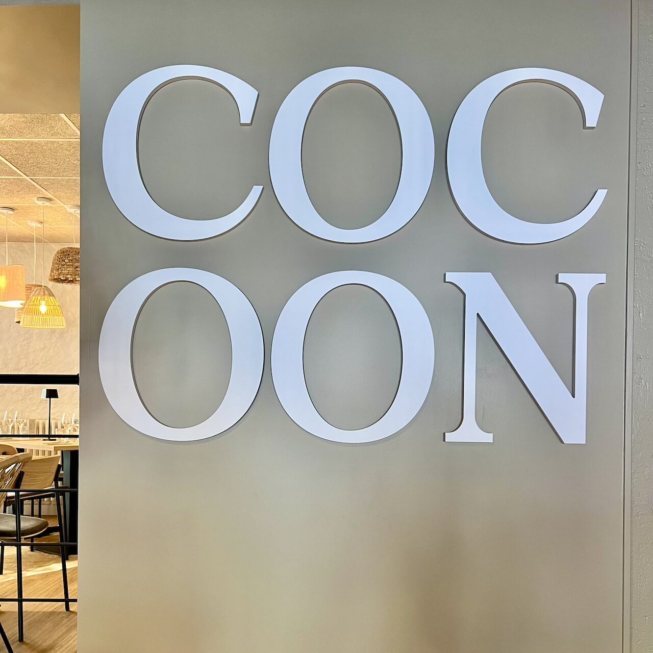 Logo blanc en relief sur fond beige, intégré avec finesse dans la salle principale