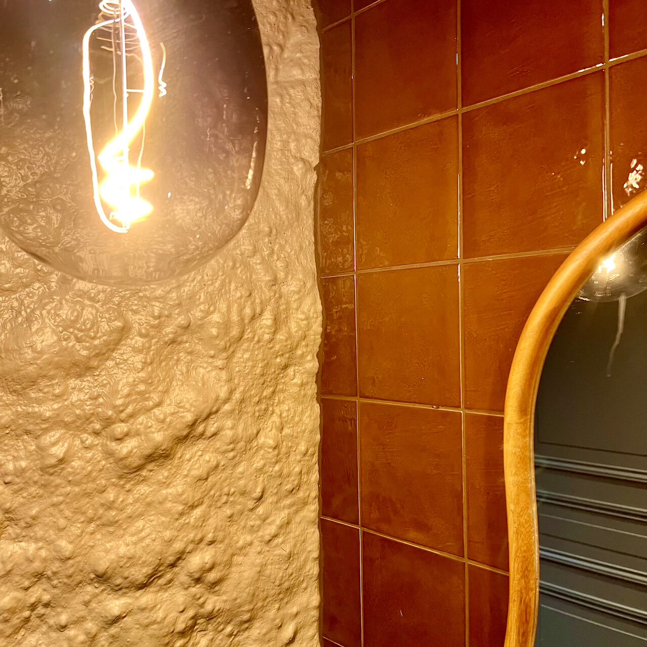 Espace sas des WC avec lumière douce, suspensions en verre fumé et faïence rappelant le bar