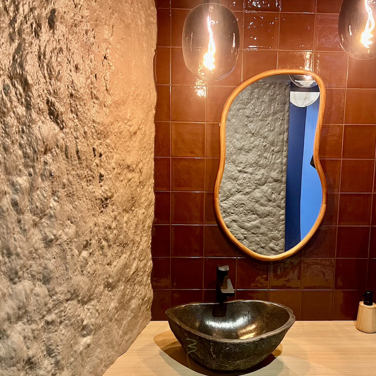 Espace sas des WC avec lumière douce, suspensions en verre fumé et faïence rappelant le bar