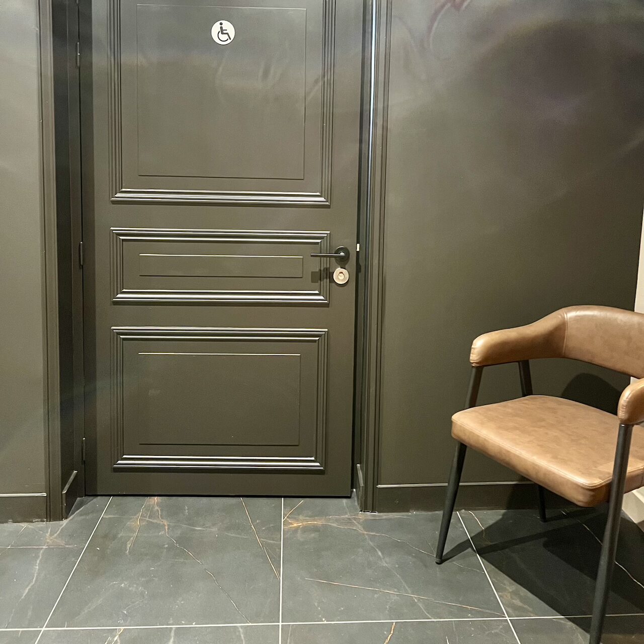 Vue de l’entrée des WC avec une porte design et un fauteuil en cuir élégant