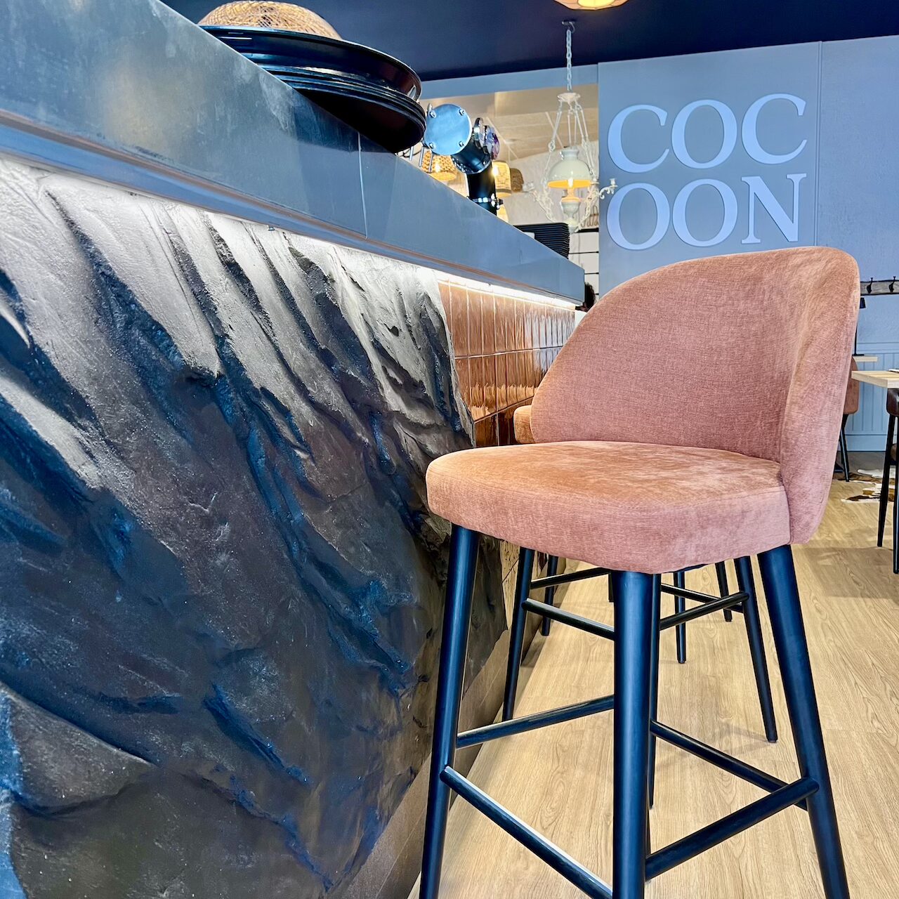 Vue sur l’habillage en pierre du bar et les mange-debout en terra cotta, espace convivial pour un verre