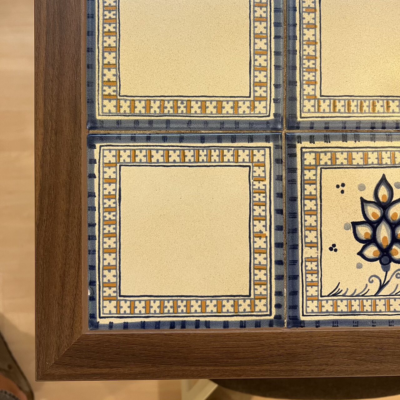 Détail des plateaux de table avec anciens plateaux faïencés réintégrés et entourages en bois, alliant tradition et modernité.