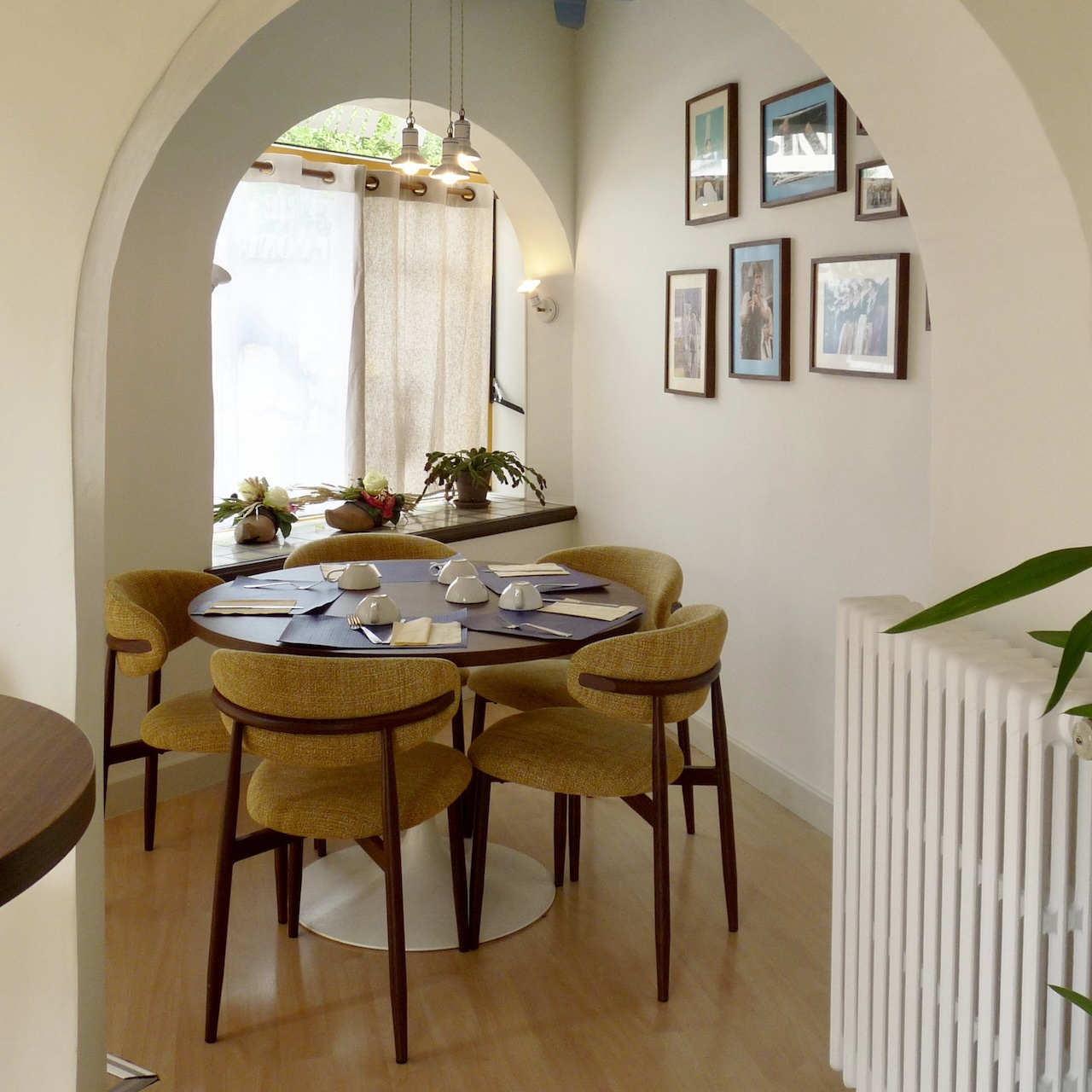 Salle arrondie ouverte sur la rue, avec des chaises jaune pastel et un plafond bleu, aménagée comme un petit salon intimiste.