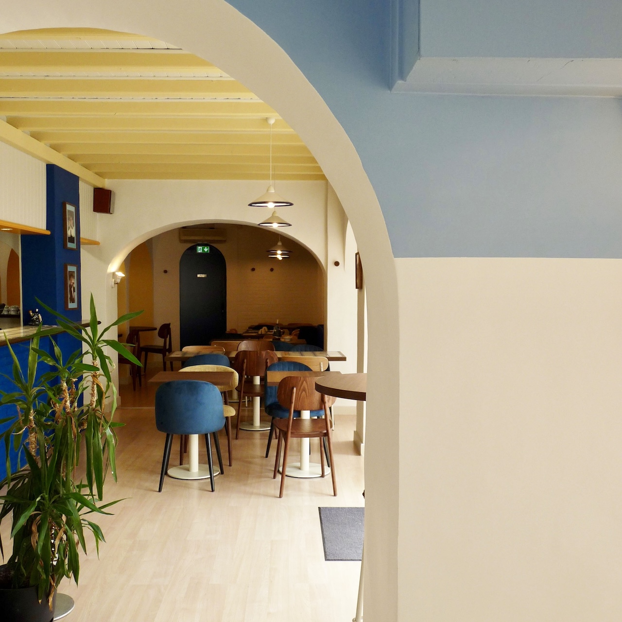 Vue profonde de la première salle de la crêperie avec poutres soulignées en jaune pâle et le bloc bleu du bar visible.