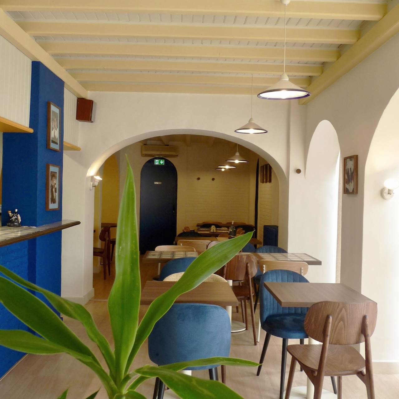 Vue profonde de la première salle de la crêperie avec poutres soulignées en jaune pâle et le bloc bleu du bar visible.