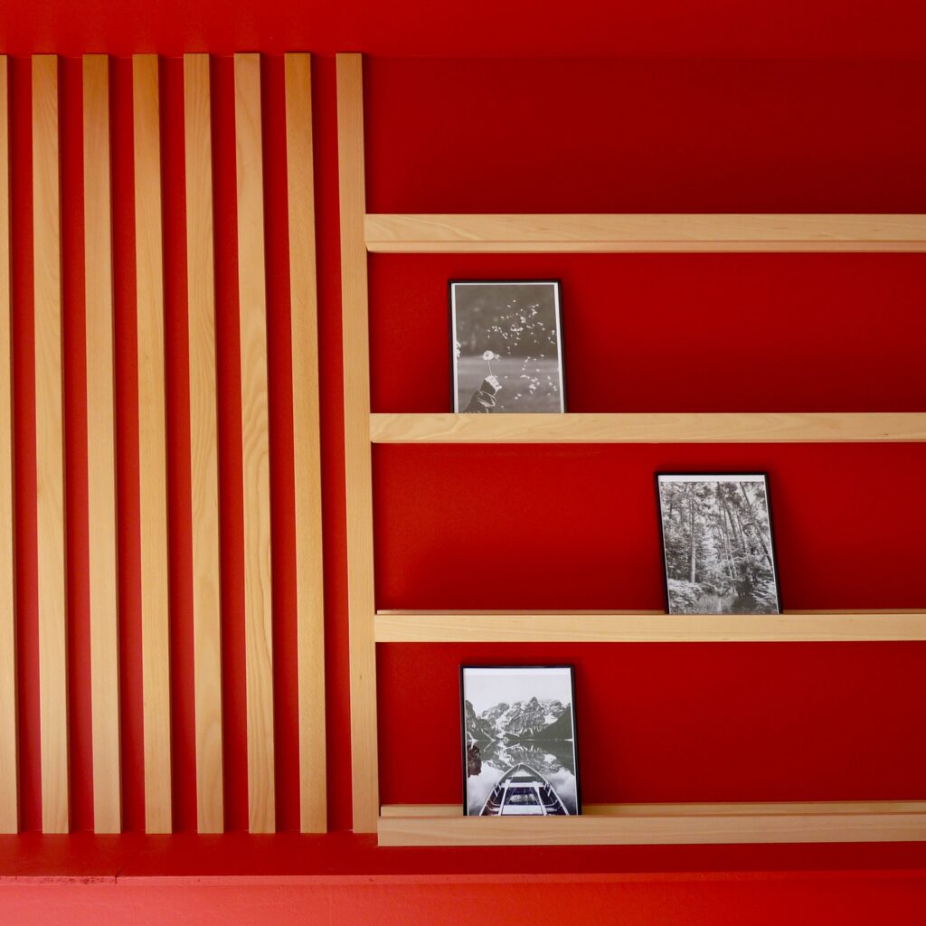 Showroom aménagé avec un mur rouge, des tasseaux en bois et une tablette pour documents commerciaux réalisés pour un artisan.