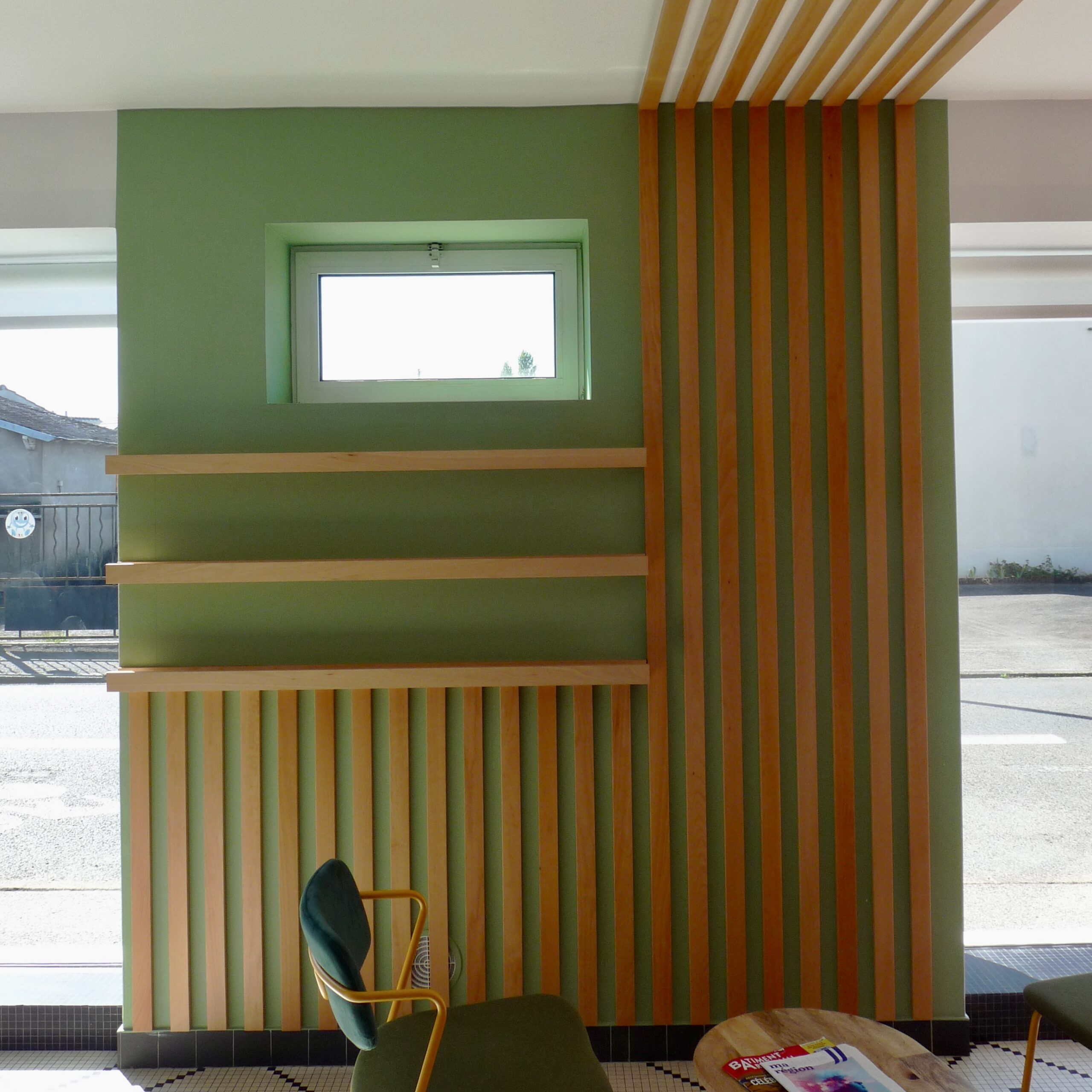 Vue de l’espace vert du showroom avec tasseaux bois et grande baie vitrée donnant sur la rue, apportant visibilité et lumière naturelle.